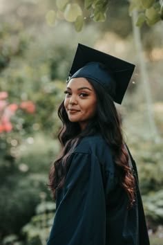 a woman wearing a graduation cap and gown standing in front of some bushes with flowers