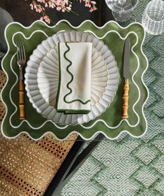 a place setting with plates, silverware and napkins on a green tablecloth