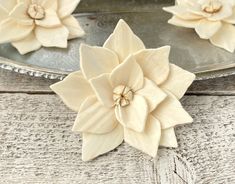 two white flowers are sitting on top of a metal platter, one is shaped like a flower and the other is made out of wood