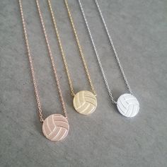 three necklaces with different designs on them sitting on top of a gray surface and one has a volleyball ball in the middle