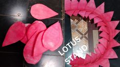 a pink wreath made out of paper on top of a black tile floor with the words lotus stand next to it