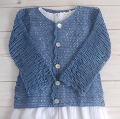 a blue knitted cardigan hanging on a white wooden wall with a dress underneath it