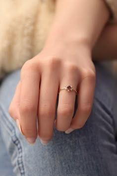 a woman's hand wearing a gold ring with a red stone on it, sitting in front of a teddy bear