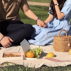 a man and woman sitting on a blanket in the grass next to some fruit,