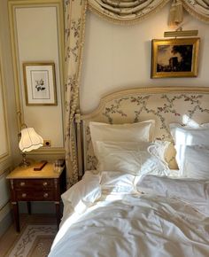 a bed with white sheets and pillows in a bedroom next to a painting on the wall