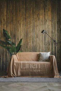 a living room with a couch covered in a linen cover and a plant next to it