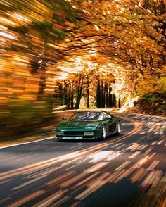 a green sports car driving down the road in front of trees with leaves on them