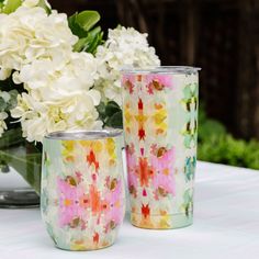 two vases sitting on top of a table with flowers in the backgroun