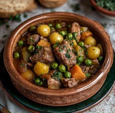 a wooden bowl filled with meat and vegetables on top of a table next to bread