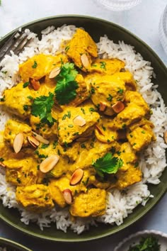 a green plate topped with chicken curry and white rice next to a bowl of cashews