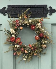 a wreath hanging on the front door of a house with dried flowers and greenery