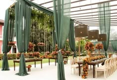 an outdoor dining area with green drapes and floral arrangements on the tables, along with hanging lanterns