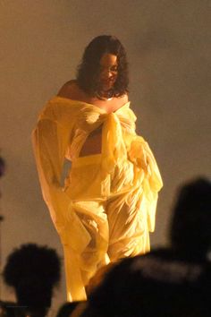 a woman in a yellow dress is standing on stage with her hands behind her back