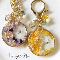 two key chains with flowers on them and the letter h in gold, white, and multicolored beads