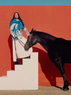 a woman standing next to a black horse on top of a white block and red wall