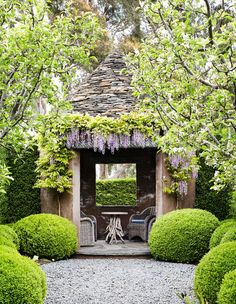 a garden with some bushes and chairs in it's center, next to a gazebo