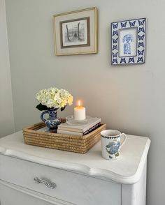 a white dresser topped with a vase filled with flowers next to a candle and books