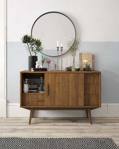 a wooden sideboard with plants and candles on it in front of a round mirror