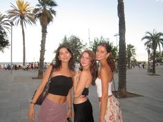 three young women standing next to each other on a sidewalk with palm trees in the background