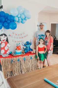 a family standing in front of a table with balloons and decorations on it at a birthday party