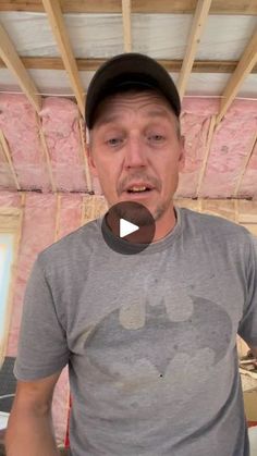 a man in a gray shirt and black hat is making a face while standing under construction