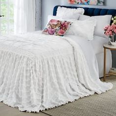 a bed with white ruffled bedspread and pink flowers on the headboard