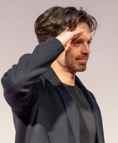 a man holding his hand to his head while standing in front of a white wall