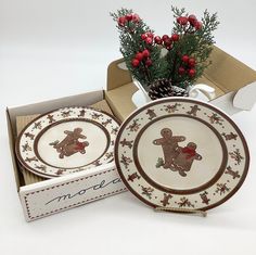 two christmas plates in a gift box next to a vase with red berries and greenery