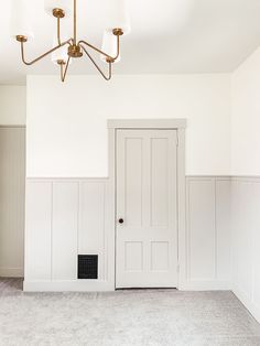 an empty room with white paneling and a light fixture hanging from the ceiling above it