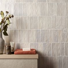 two vases with flowers in them sit on a shelf next to a tiled wall