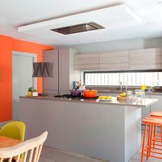 a kitchen with orange and gray walls, white counter tops and wooden bar stools