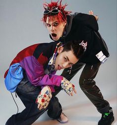 two young men posing for a photo in front of a gray background, one with red hair and the other with blue eyes