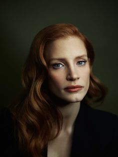 a woman with red hair and blue eyes looks into the camera while wearing a black jacket