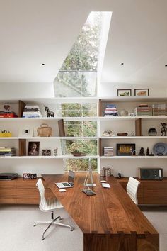 a wooden desk sitting under a skylight in a room with bookshelves and shelves