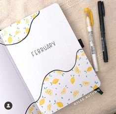 an open planner with lemons on it next to two pens