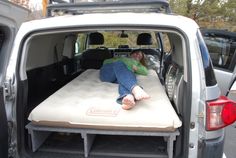 a person laying on top of a mattress in the back of a truck with its trunk open