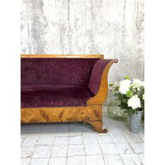 a wooden couch sitting next to a vase with flowers in it on a tile floor