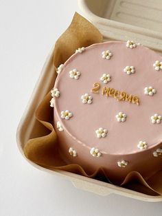 a pink cake with white flowers and the words 2 vecino written on it in gold lettering