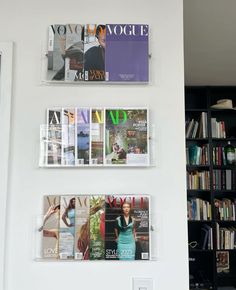 three magazines are hanging on the wall next to a bookcase with books in it