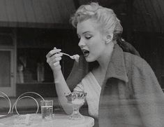 a woman sitting at a table with a spoon in her mouth while eating from a bowl