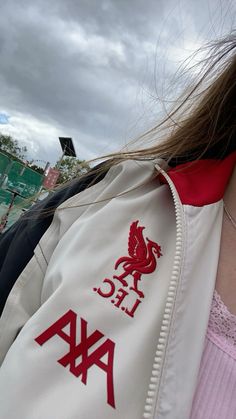 a close up of a person wearing a white jacket and red collared shirt with the liverpool football club logo on it