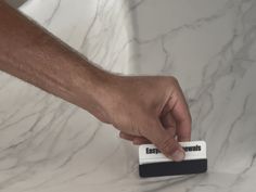 a hand is pressing the button on a white marble counter top with black and white trim