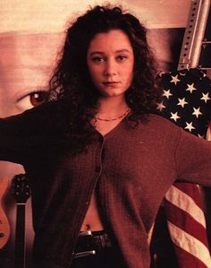 a woman standing in front of an american flag with her hands on her hips and holding a guitar