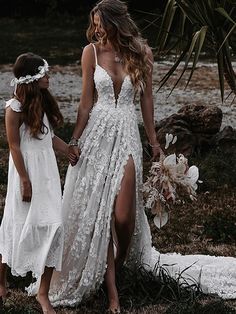 two women in white dresses holding hands while standing next to each other on the grass