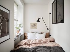 a bed sitting under a window next to a wall mounted lamp and framed pictures on the wall