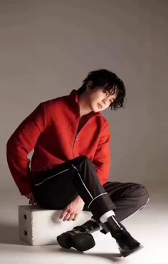 a man sitting on top of a white box wearing black boots and a red jacket