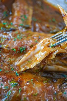 a fork is stuck into some meat with gravy and parsley on it