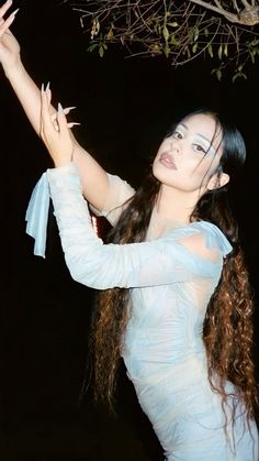 a woman with long hair wearing a white dress and holding her arms up in the air