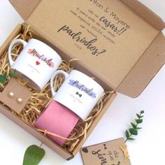 two coffee mugs sitting in a box on top of a white table next to a plant