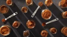 several jars filled with different types of spices and spoons next to each other on a table